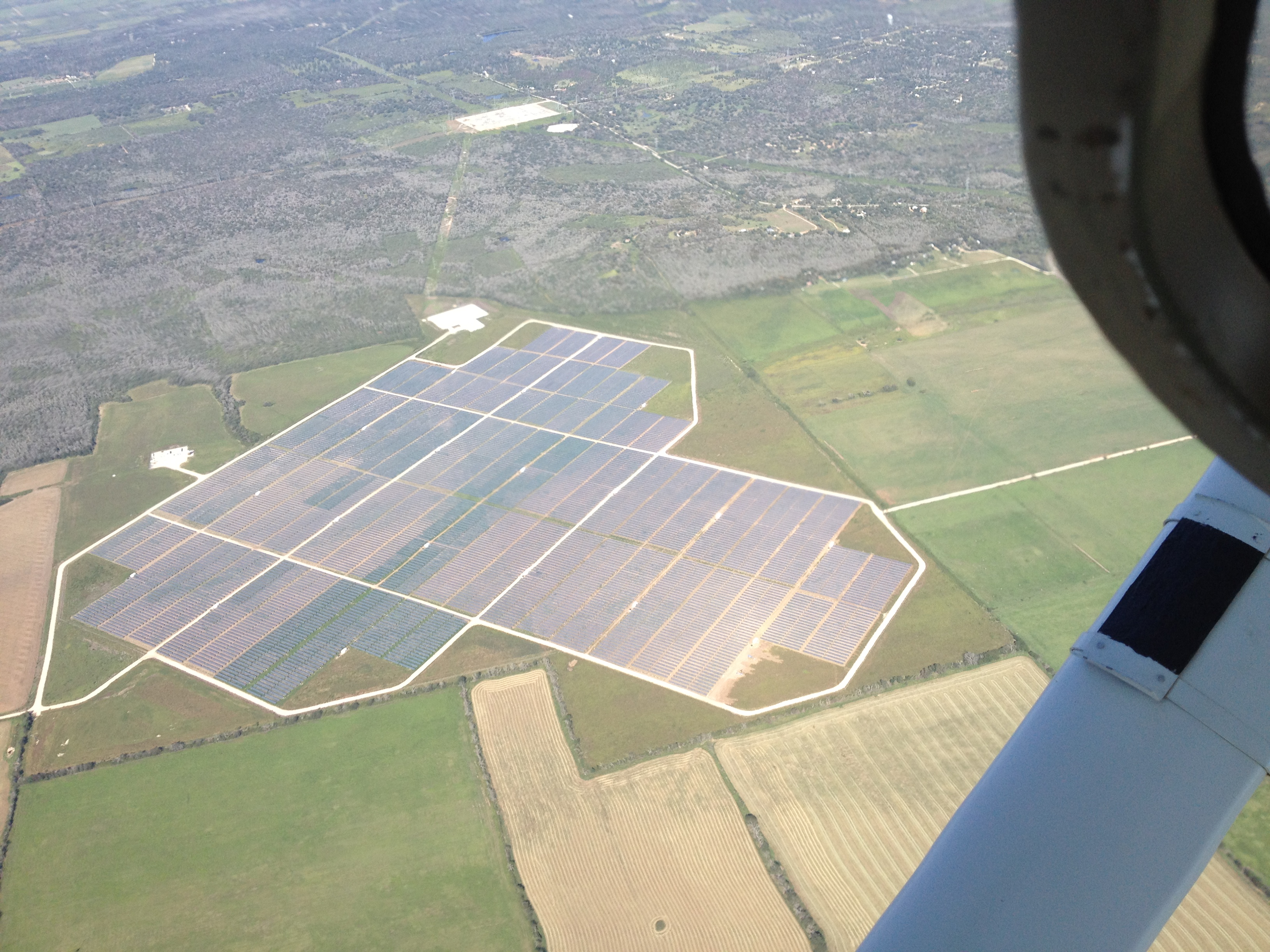 Repeated blocks of solar panels and access roads at Webberville Solar Farm, seen from an aircraft