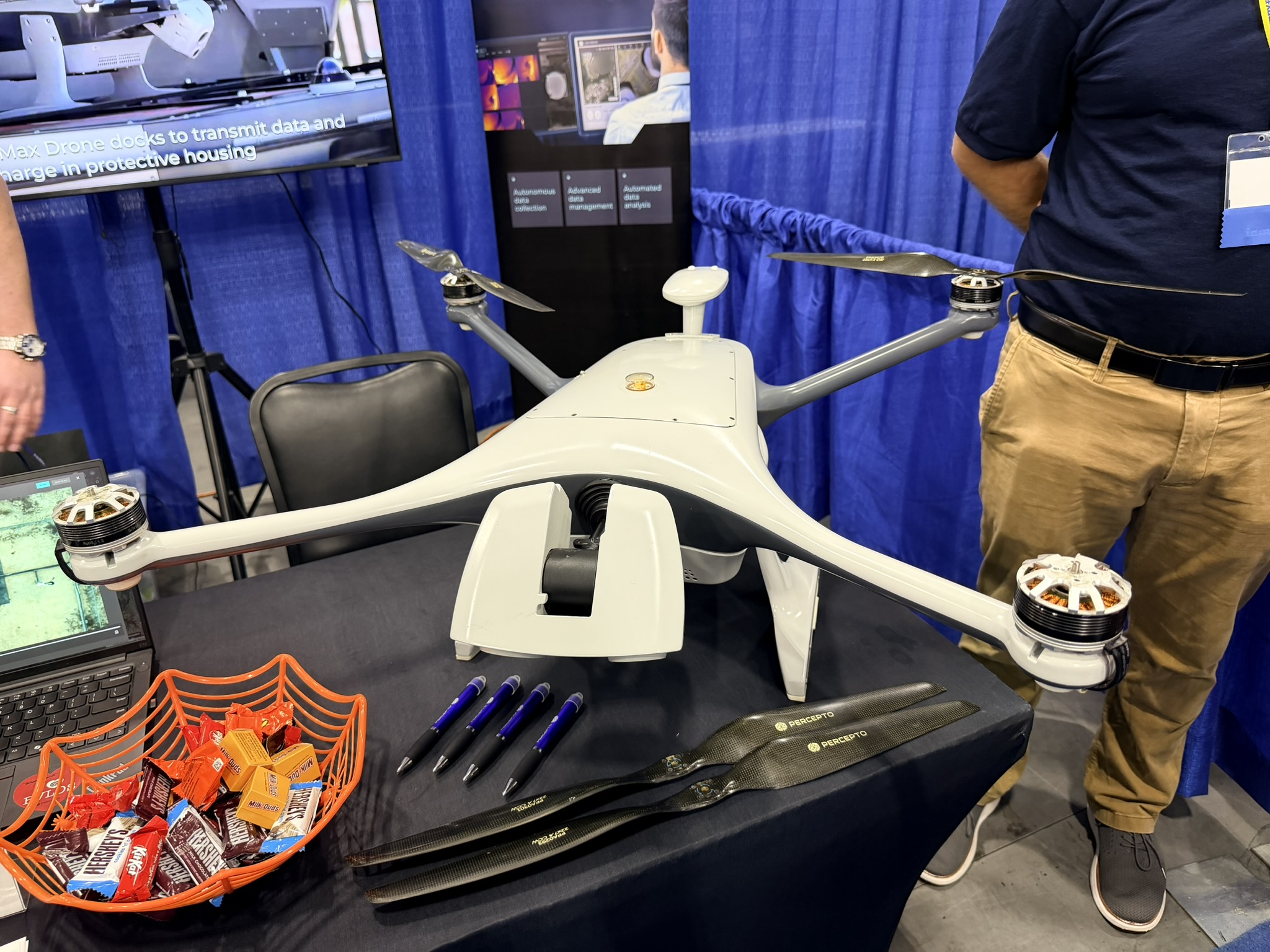 Percepto Sparrow quadcopter on an indoor display table beside a laptop and a screen showing its docking enclosure.