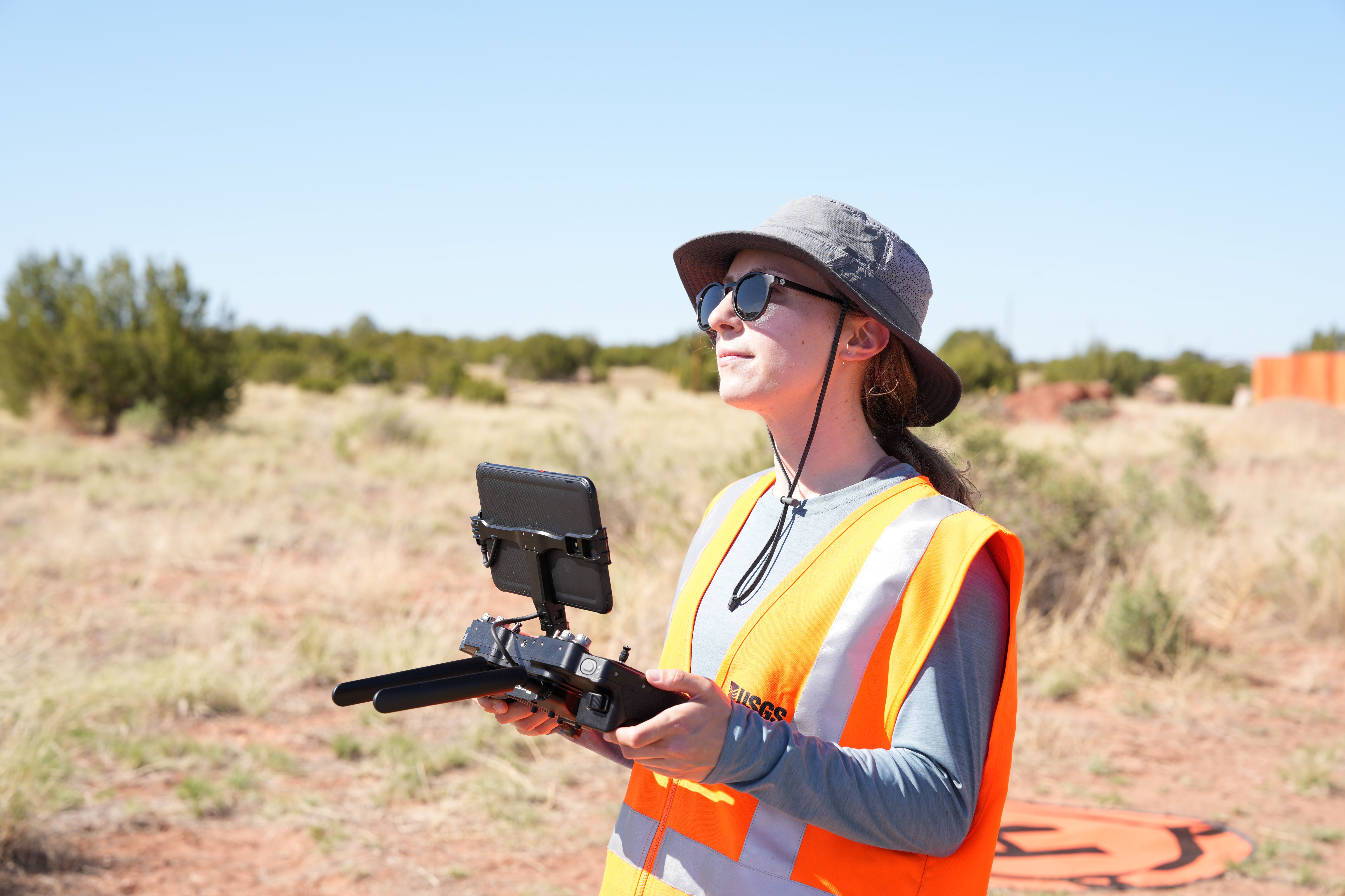 USGS drone pilot in a safety vest holding a controller with a mounted screen during outdoor mapping work