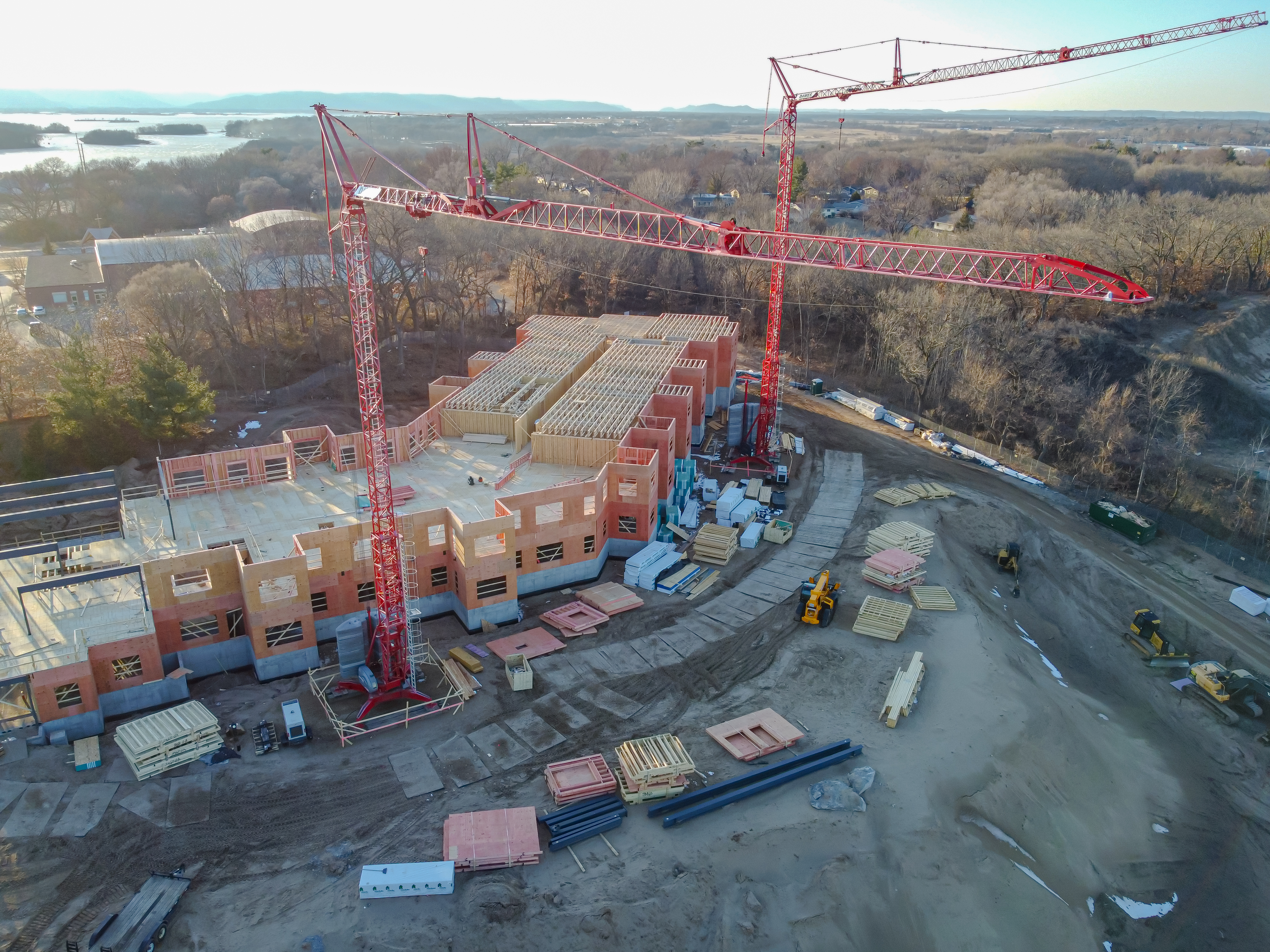 Aerial view of red tower cranes, a partially framed building, access routes, and stacks of construction materials.