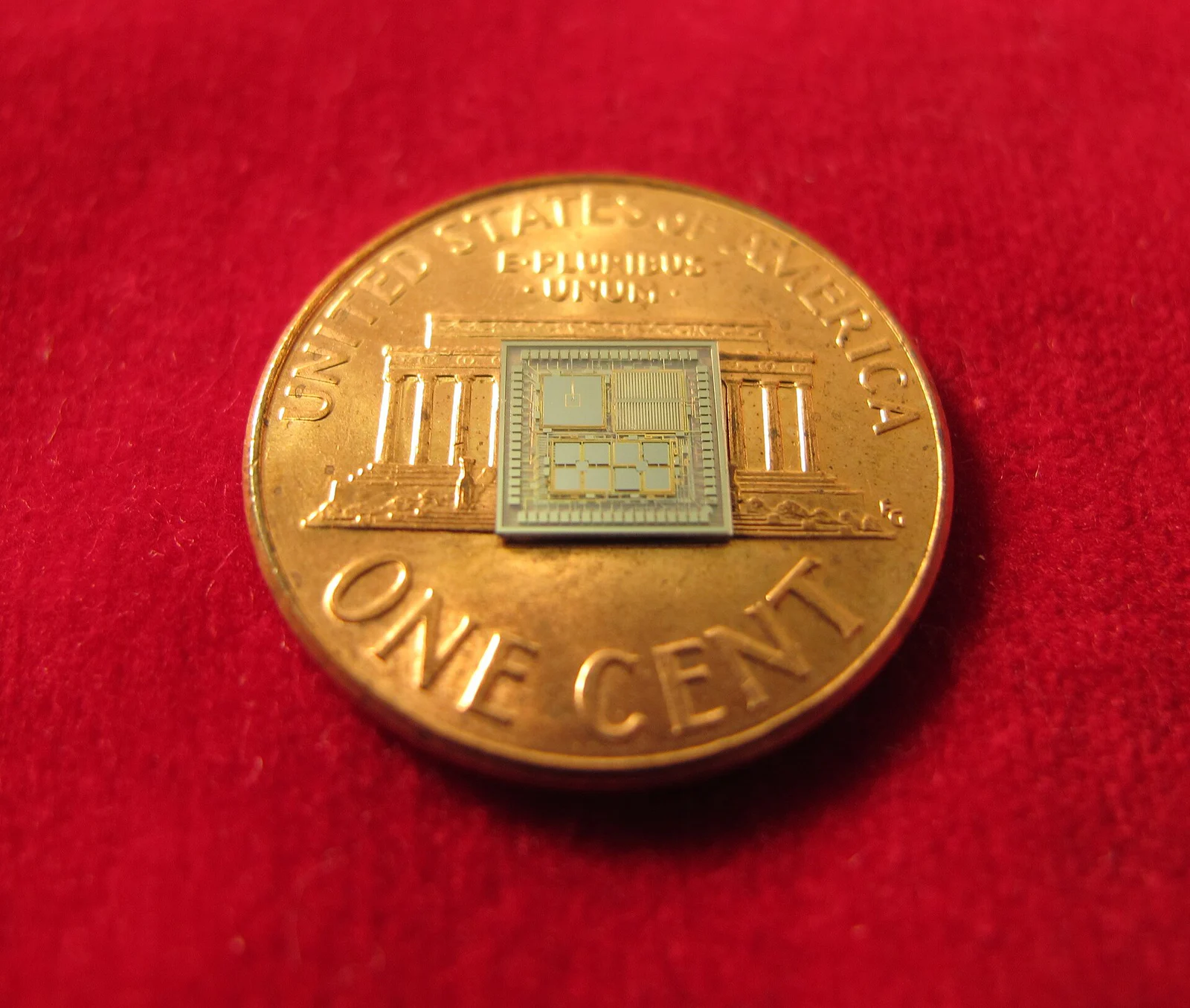 A miniature DARPA timing and inertial measurement prototype resting on a U.S. penny for scale.