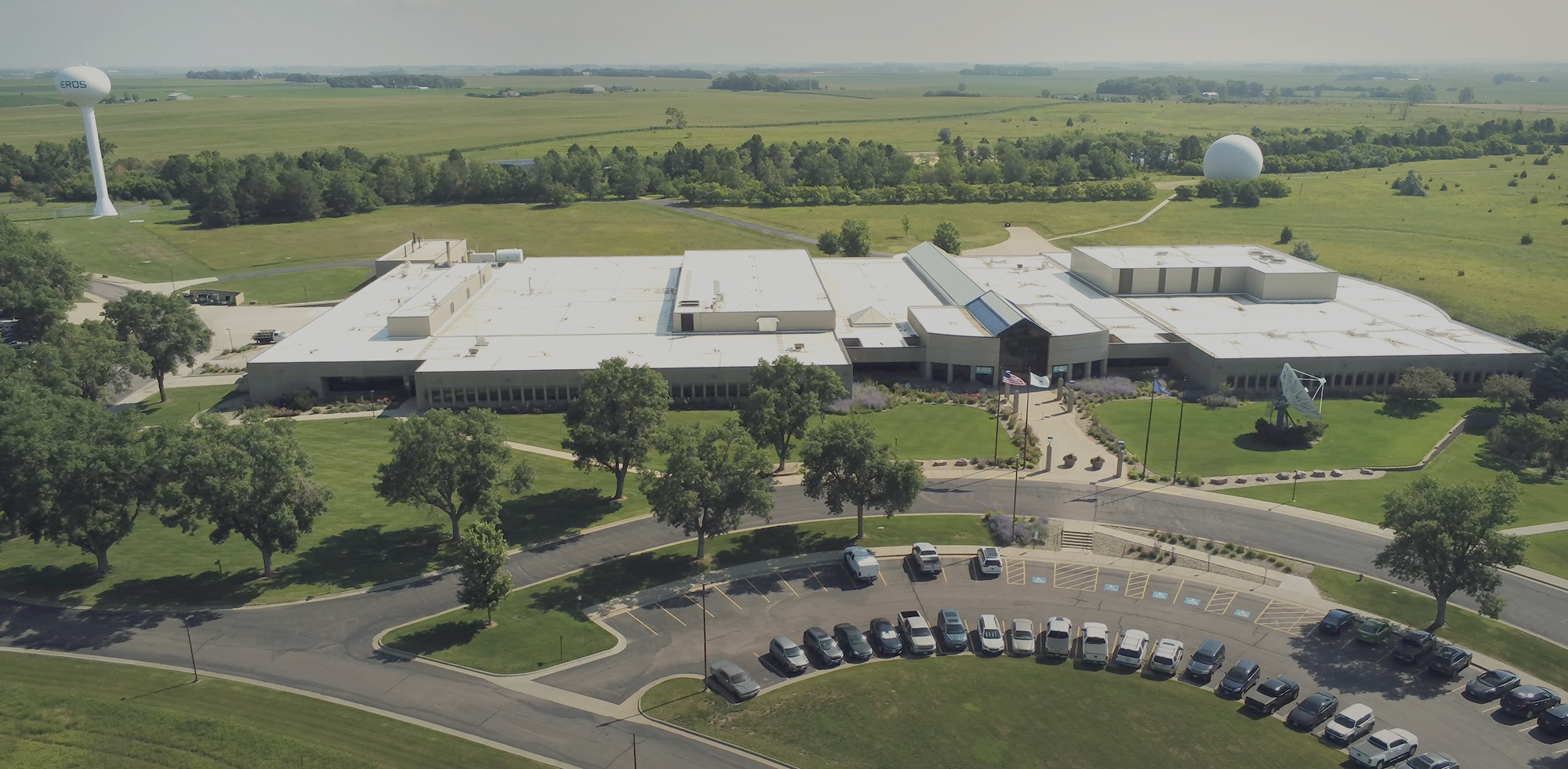 Oblique aerial view of the USGS EROS Center showing its broad roof, front facade, trees and parking area.