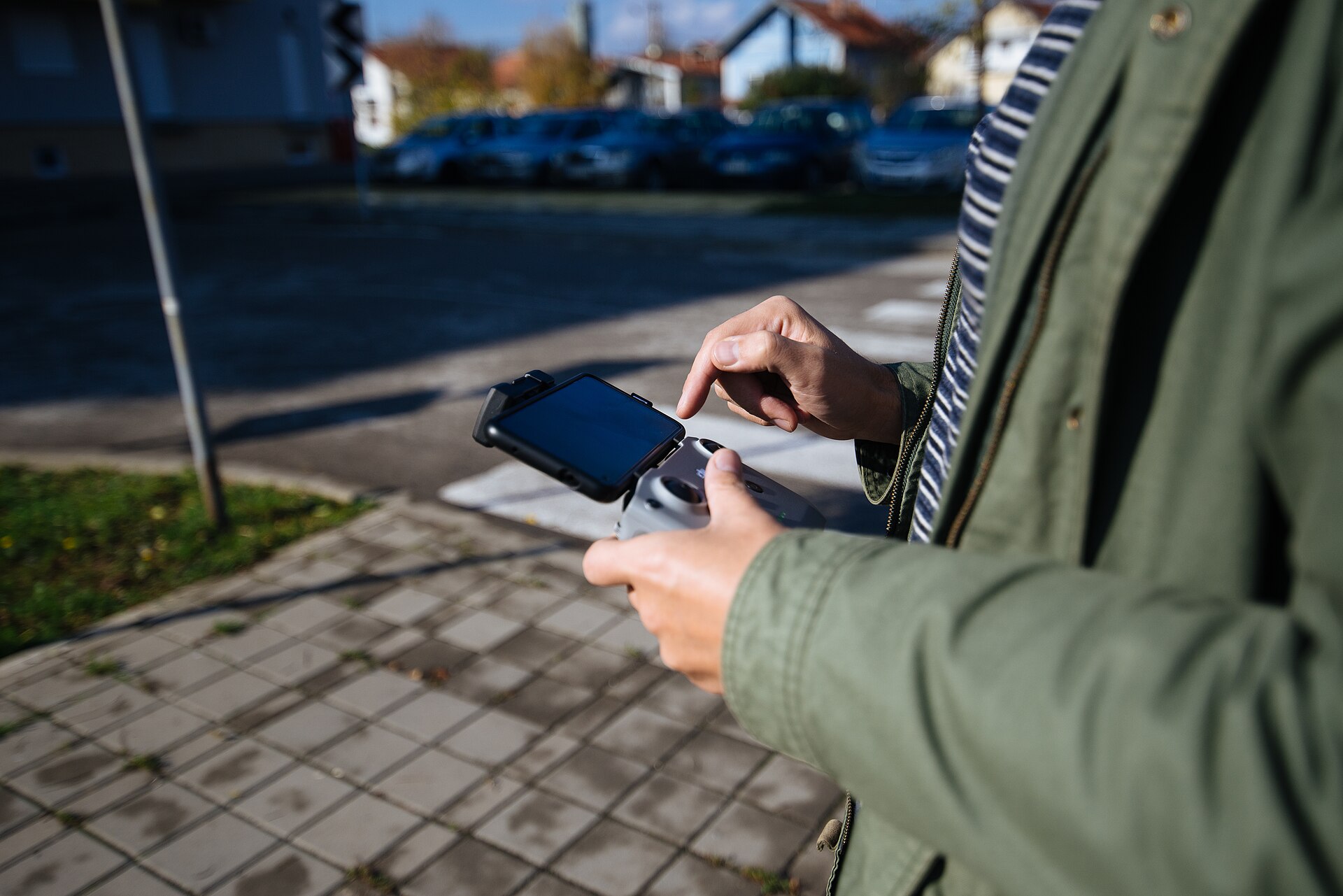 A person holds a drone controller with a mounted smartphone and touches the phone screen outdoors.
