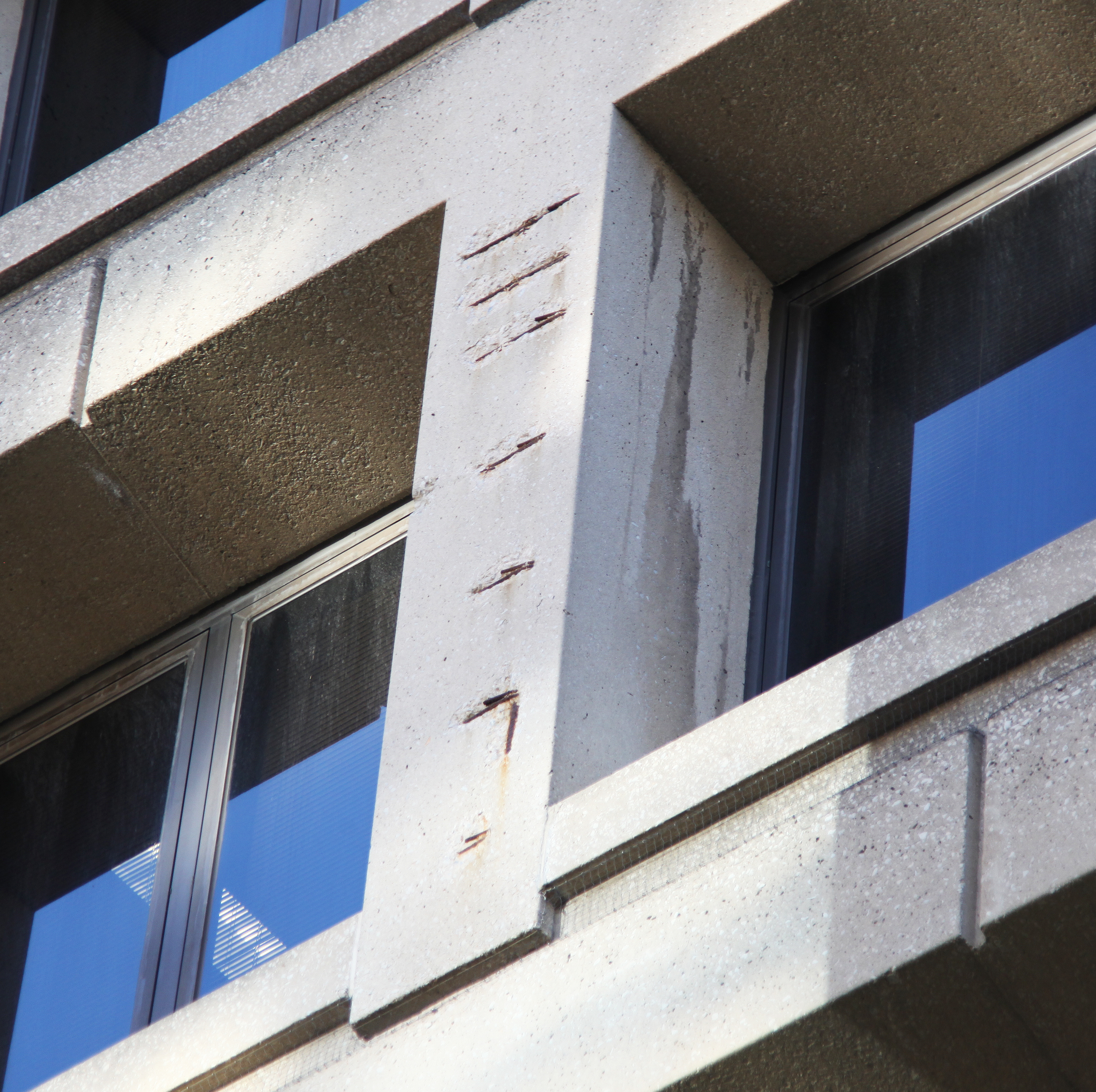 Missing concrete and rust-colored marks along a vertical facade member between recessed windows.