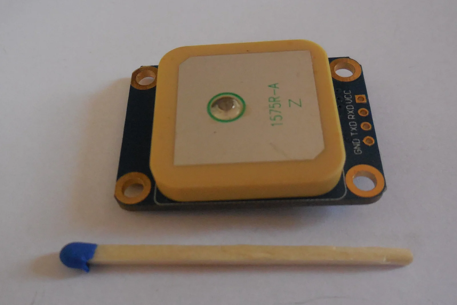 A GNSS receiver module with an integrated patch antenna and exposed power and serial connection pads.