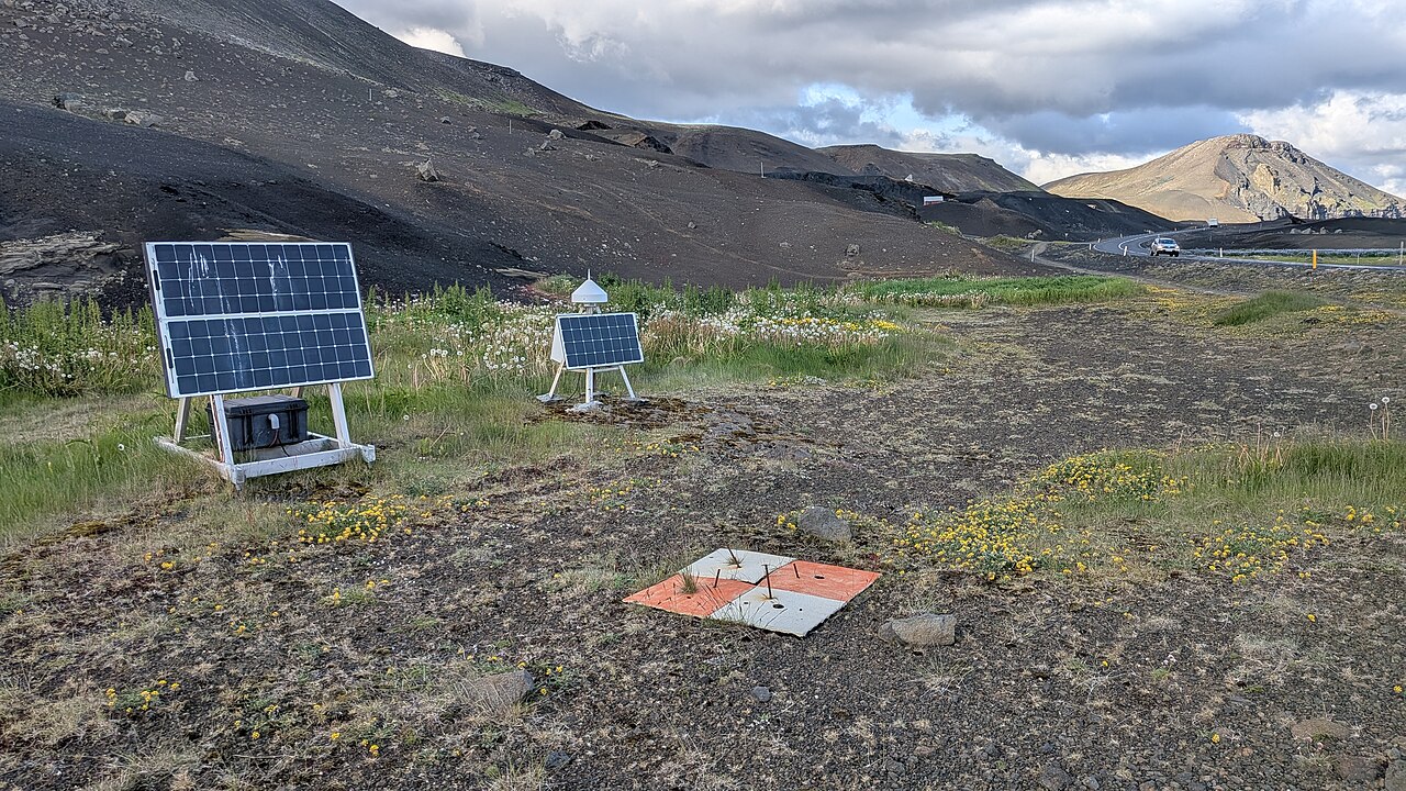 Orange-and-white ground target beside solar-powered field instruments on rocky terrain in Iceland