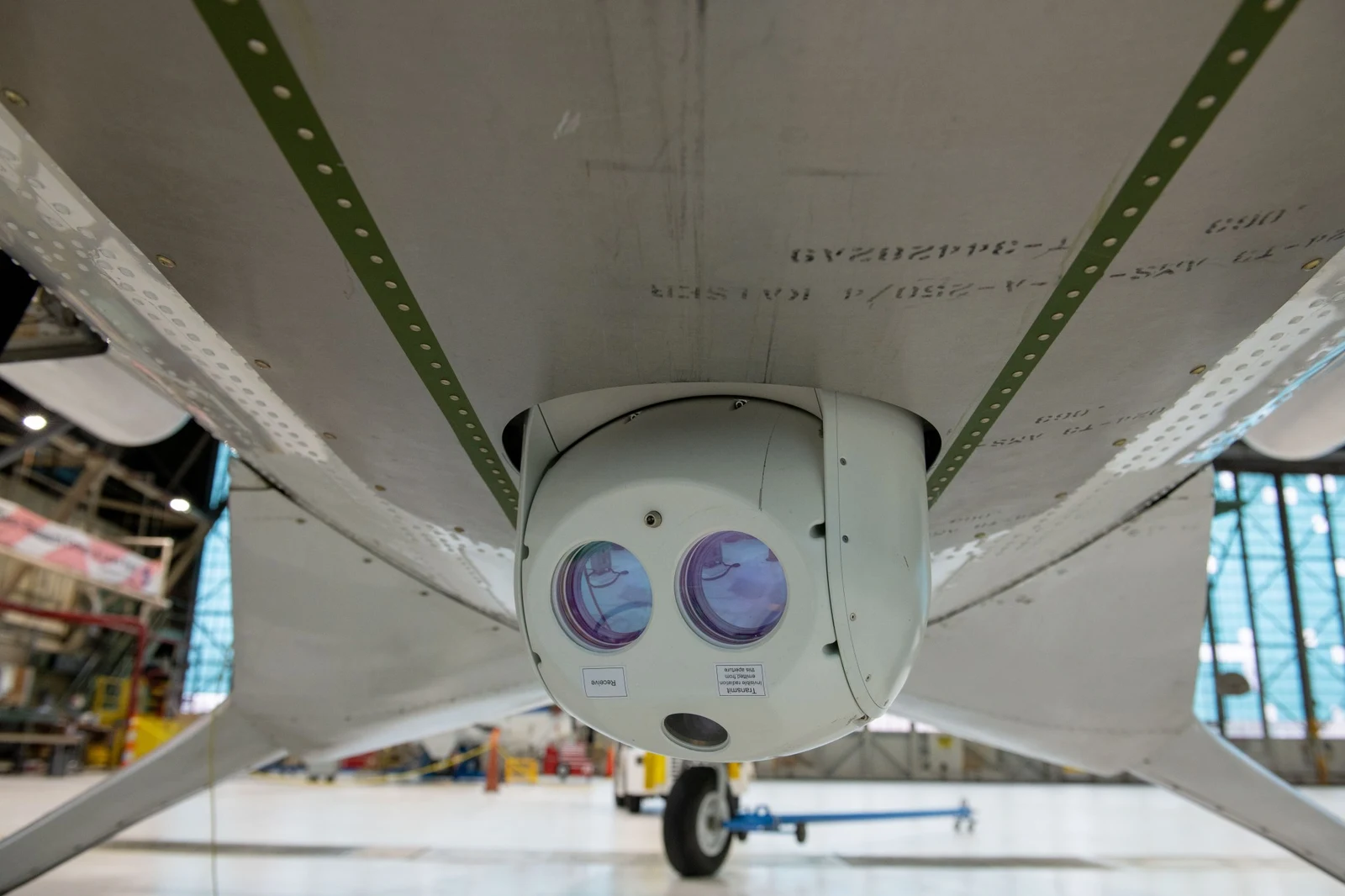 NASA optical communications hardware mounted beneath the wing of a Twin Otter research aircraft inside a hangar.