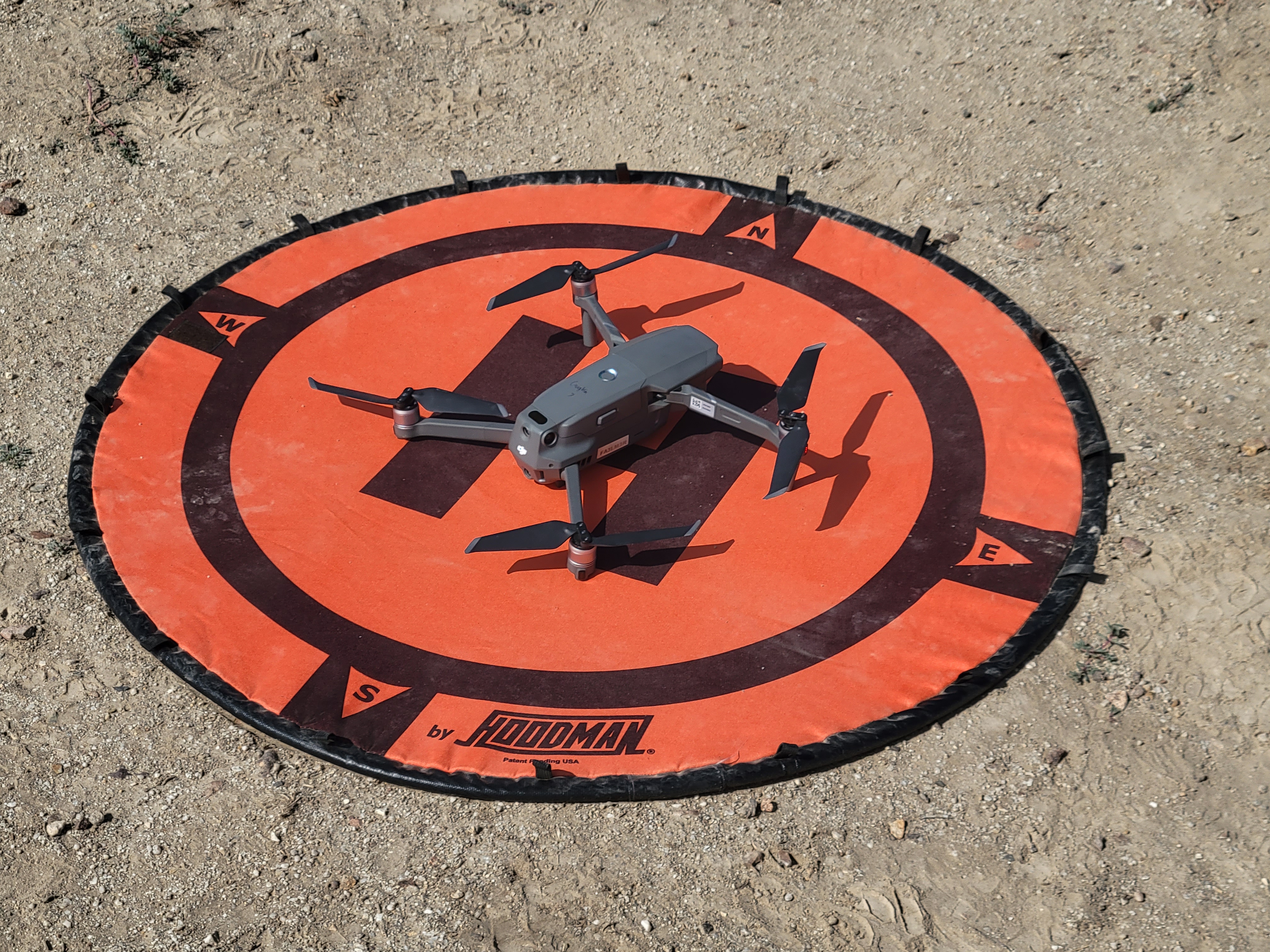 Quadcopter resting on an orange landing pad at a field site