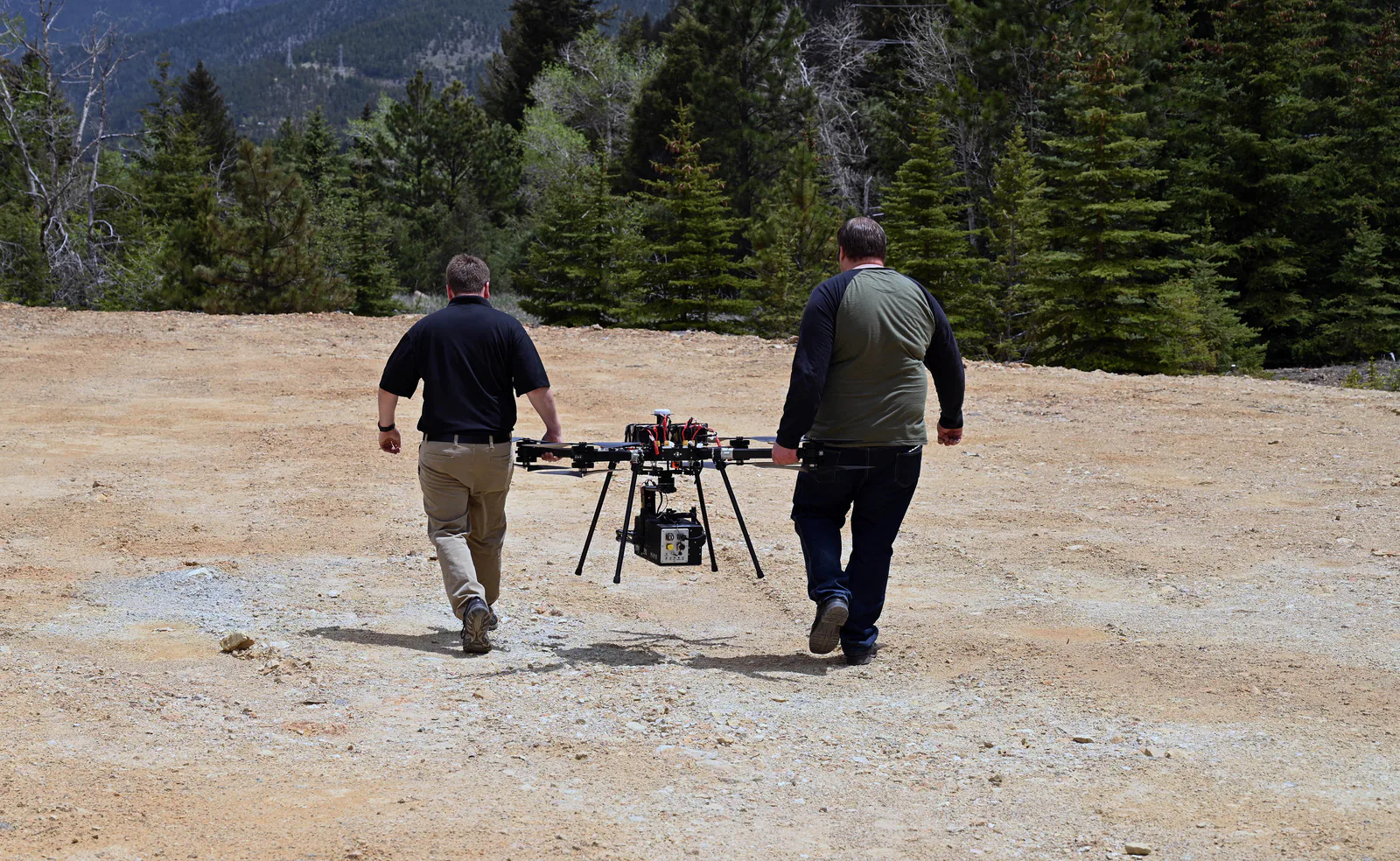Two field team members carry a multirotor UAS with a hyperspectral camera mounted beneath it.